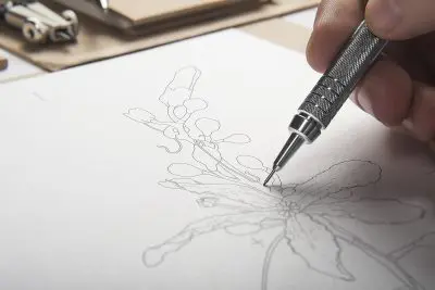 Hand sketching an intricate floral design with a fine pen on paper.